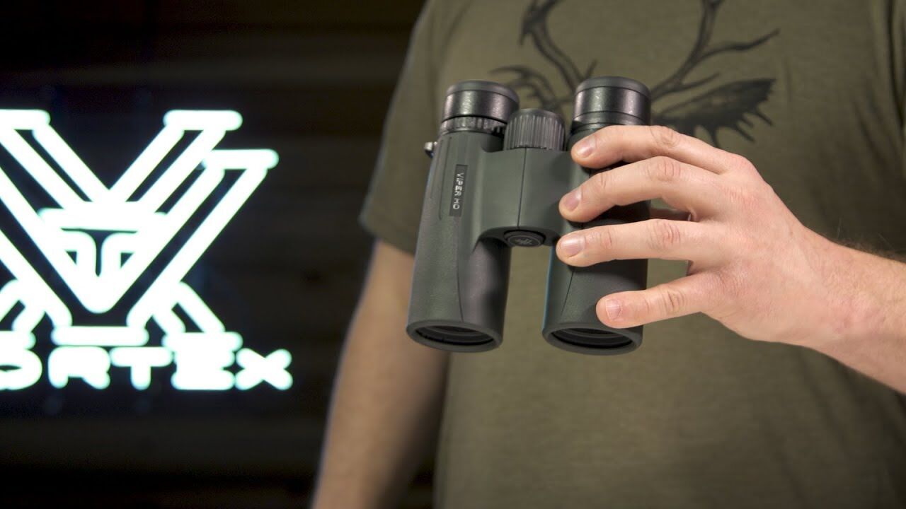 Eine Person hält ein grünes Fernglas, im Hintergrund ist das Logo von Vortex sichtbar