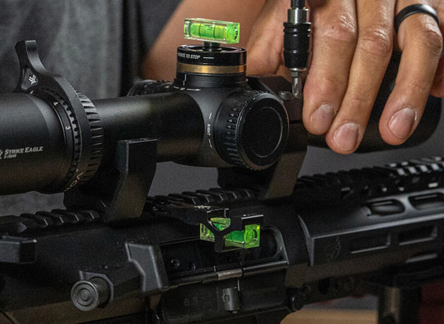 Eine Person richtet ein Zielfernrohr mit einer Wasserwaage auf einem Gewehr präzise aus.
