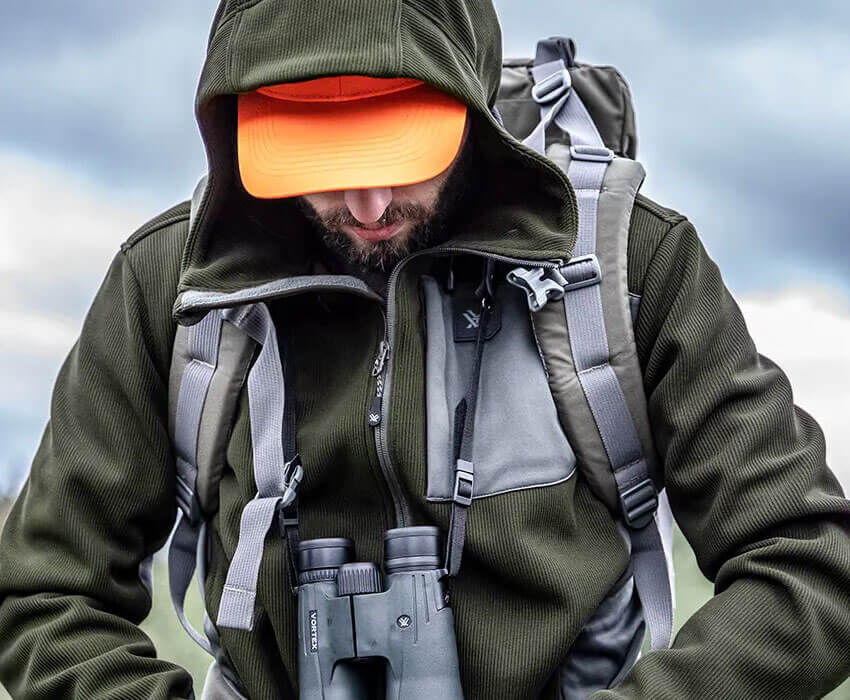 Mann in Outdoor-Jacke mit Rucksack und Fernglas, bereit für Erkundungen