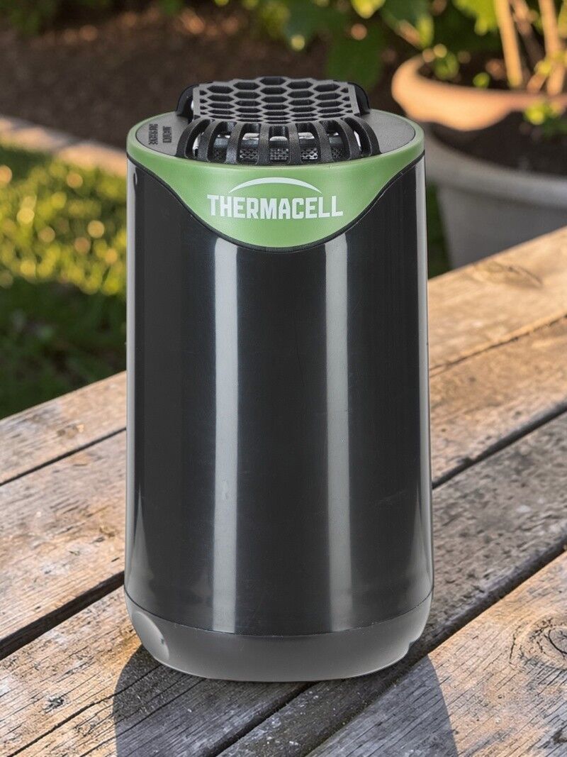 Schwarzes Thermacell Mückenschutzgerät steht auf einem Holztisch im Garten und bietet schnurlose Mückenabwehr für Terrasse und Outdoor-Bereiche