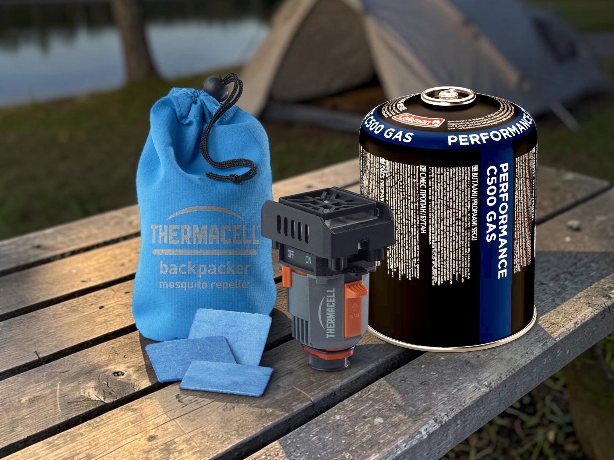 Thermacell Backpacker Mückenschutzgerät mit blauer Transporttasche, Wirkstoffpads und Coleman G500 Gaskartusche auf Holztisch vor Zelt beim Camping