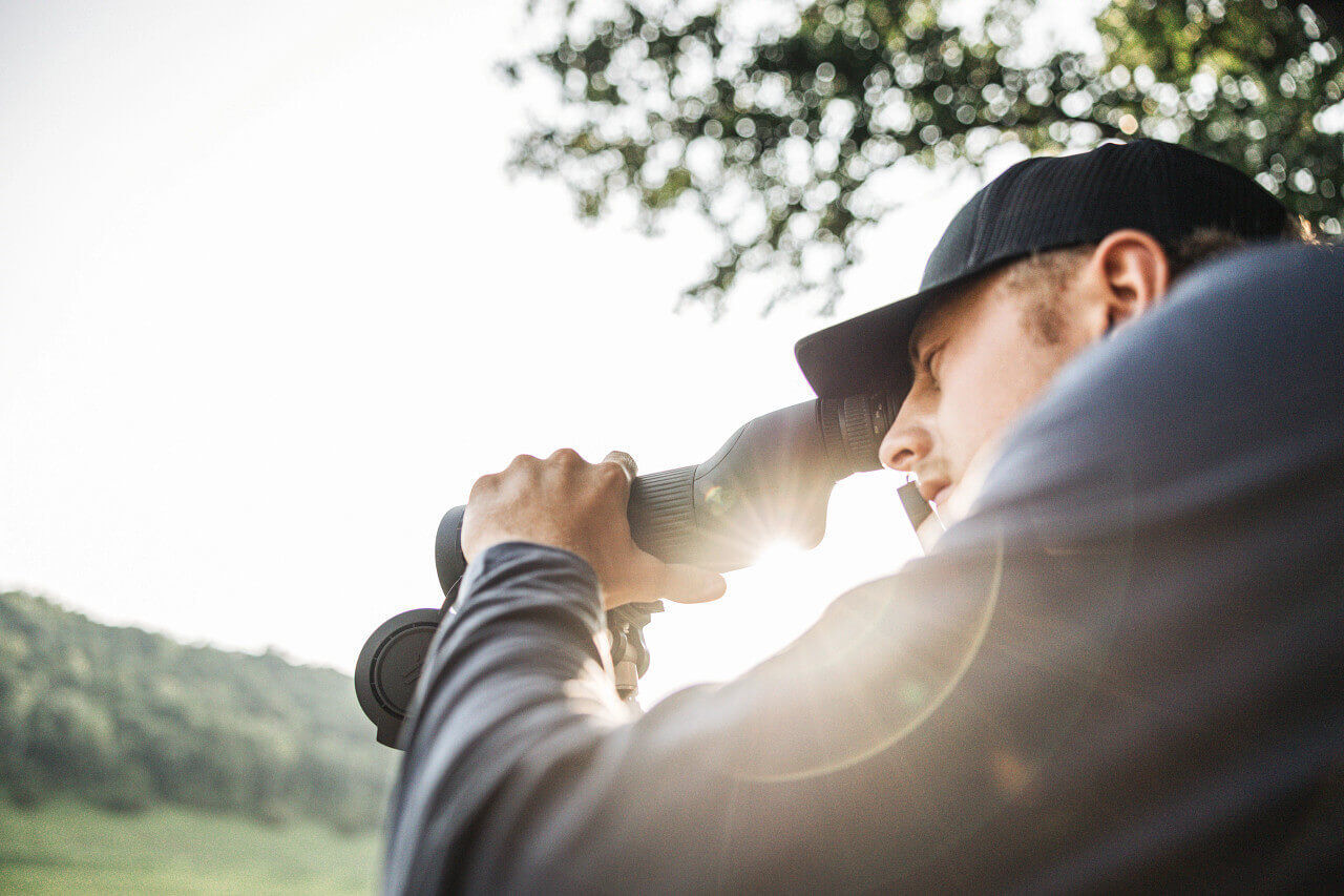 Mann mit Baseballmütze nutzt Fernglas in einem grünen Waldgebiet