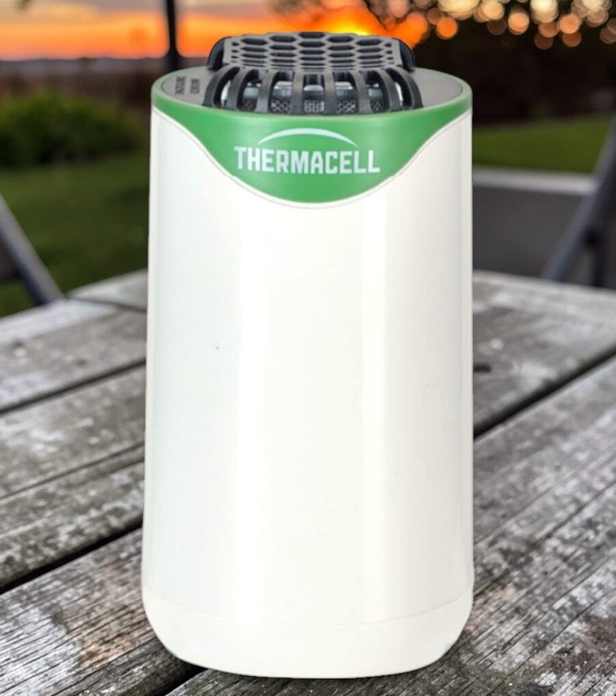 Weißes Thermacell Mückenabwehrgerät steht auf einem Holztisch im Garten bei Sonnenuntergang