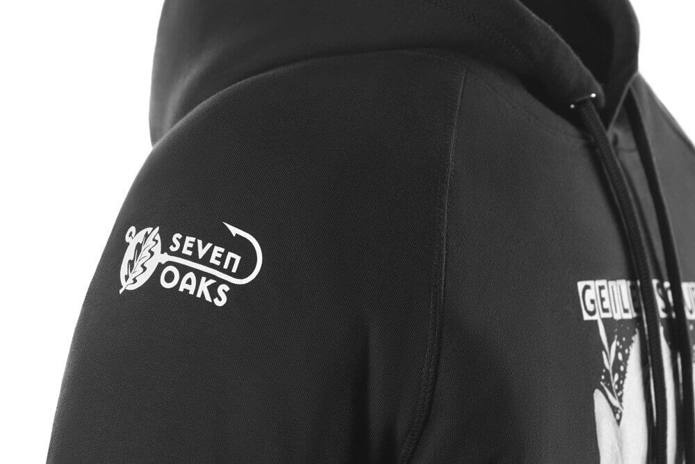 Nahaufnahme eines schwarzen Hoodies mit Seven Oaks Logo auf dem Ärmel, Kapuze und Kordeln sichtbar
