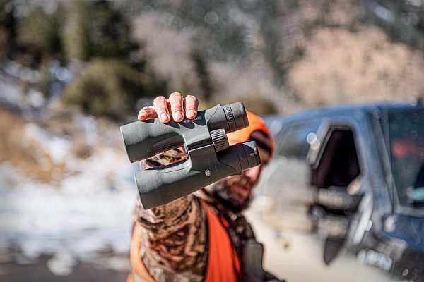 Person hält ein Fernglas vor winterlicher Landschaft hoch