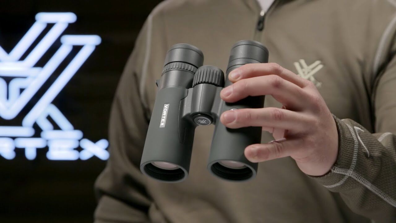 Person hält ein modernes Fernglas mit griffigem Design vor einem Firmenlogo