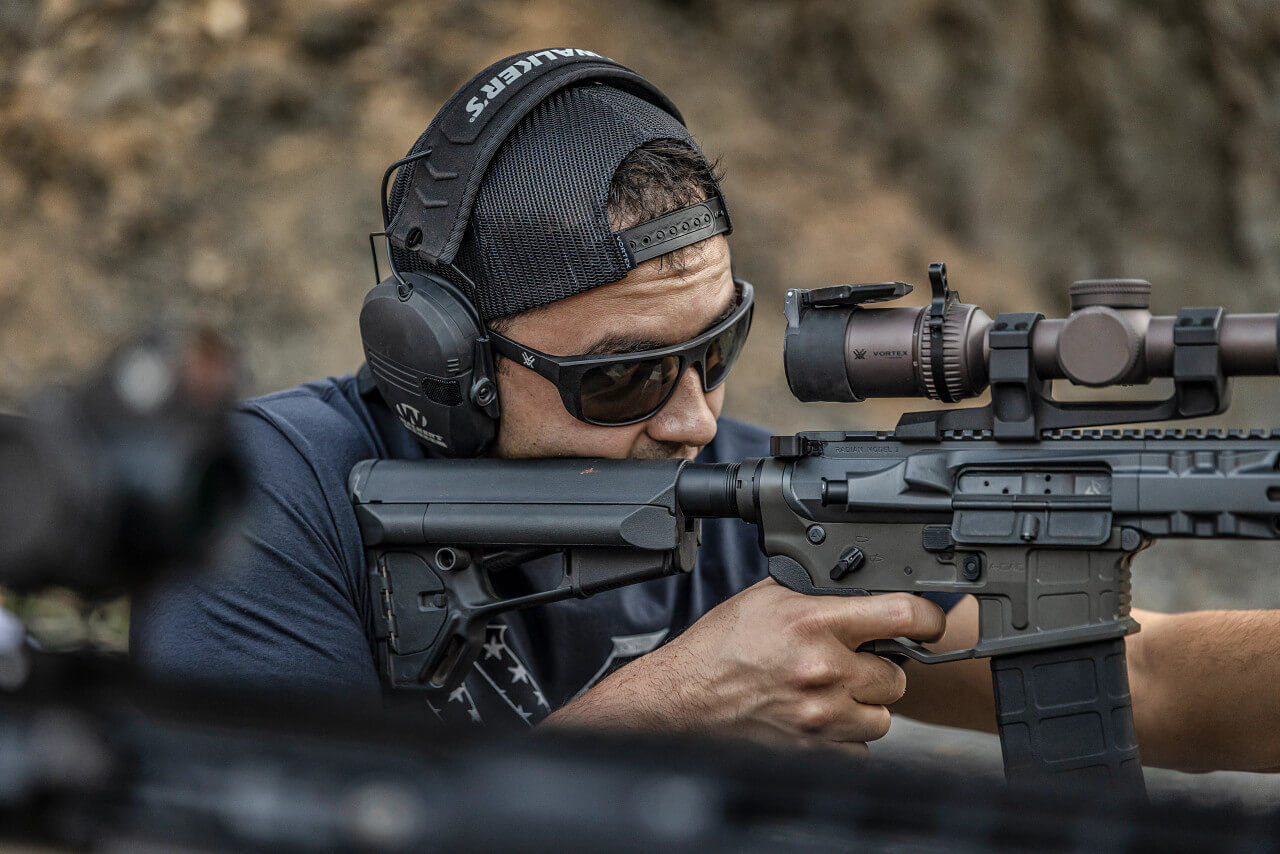 Mann mit Sonnenbrille und Kopfhörern zielt mit einem Gewehr im Freien