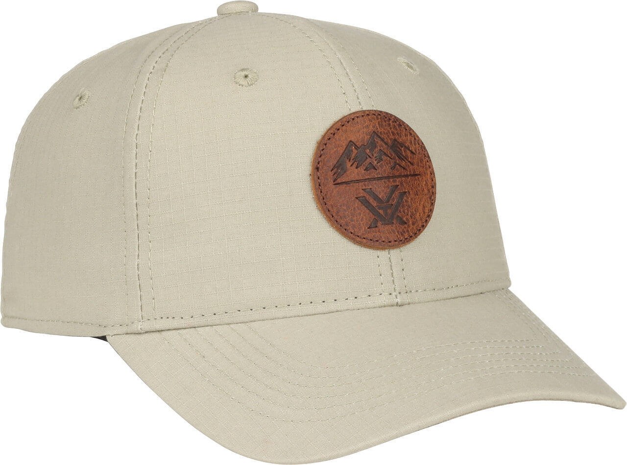 Beige Schirmmütze mit rundem Leder-Emblem und Bergmotiv, seitliche Ansicht