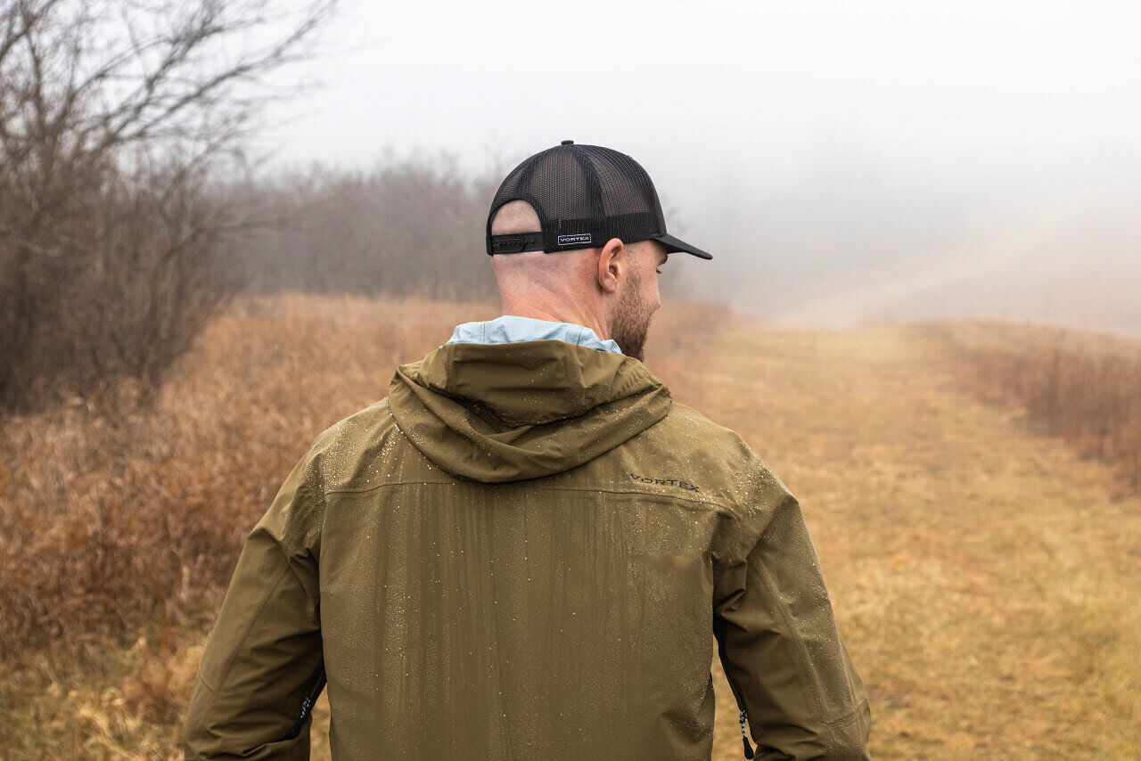Rückansicht eines Mannes mit Baseballkappe und Regenjacke auf einem nebligen Pfad