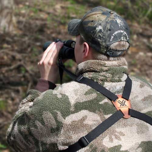 Person in Camouflage-Jacke und Baseballmütze beobachtet mit Fernglas im Wald