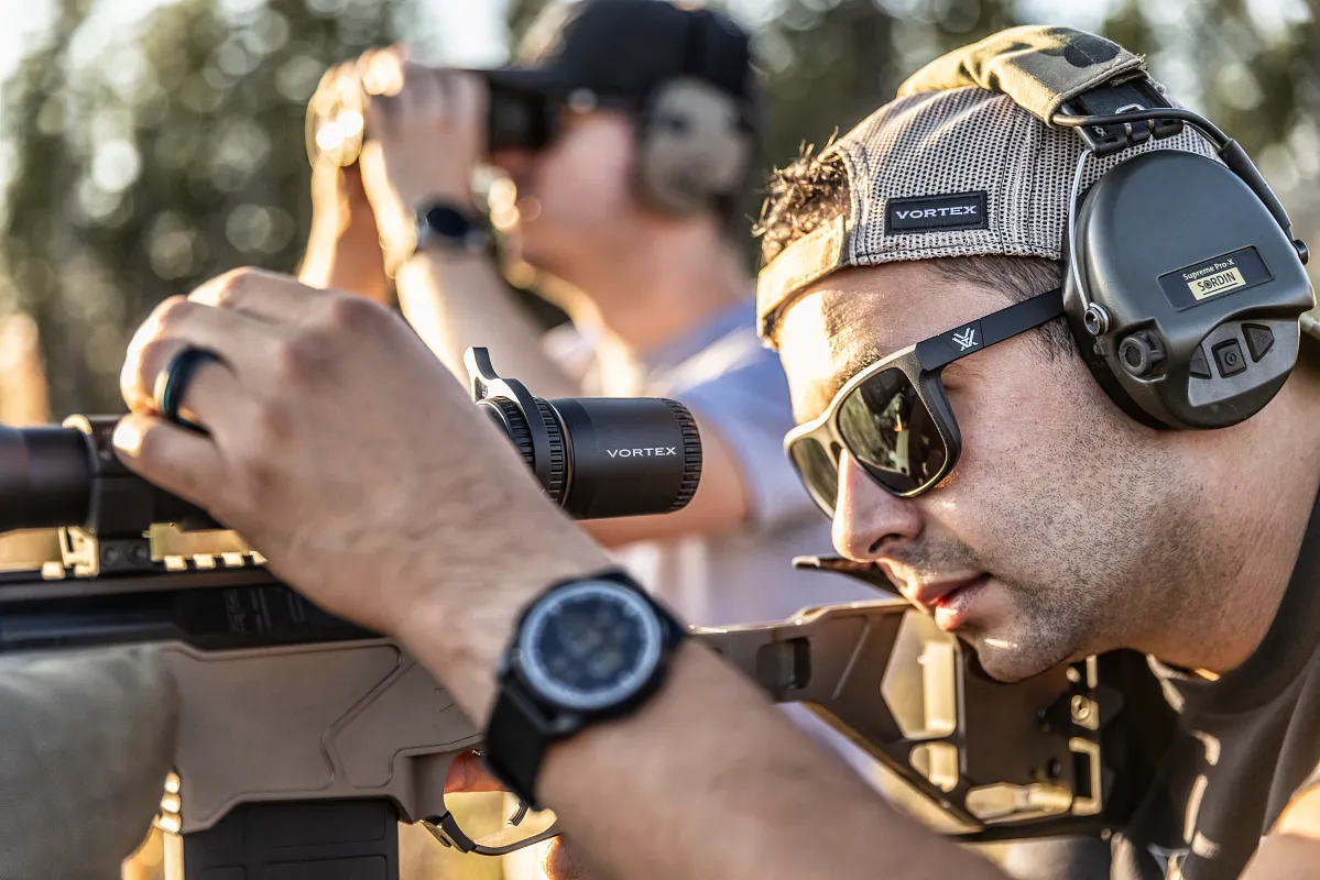 Nahaufnahme eines Mannes beim Zielen mit einem Gewehr, trägt Gehörschutz und Sonnenbrille