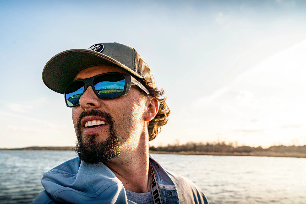 Mann trägt Sonnenbrille und Kappe, genießt sonnigen Tag am Wasser