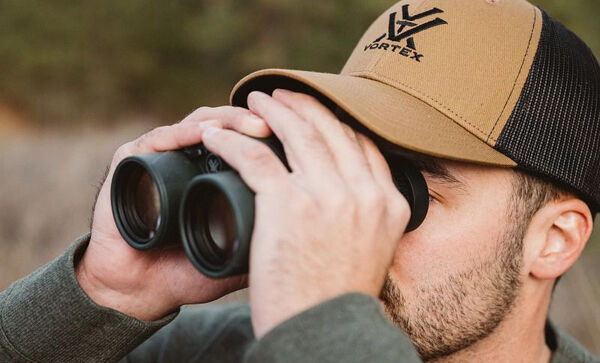 Ein Mann mit brauner Kappe schaut durch ein Fernglas in einer natürlichen Umgebung