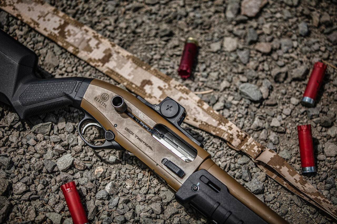 Nahaufnahme einer Beretta 1301 Tactical Schrotflinte, umgeben von roten Schrotpatronen auf Kieselboden