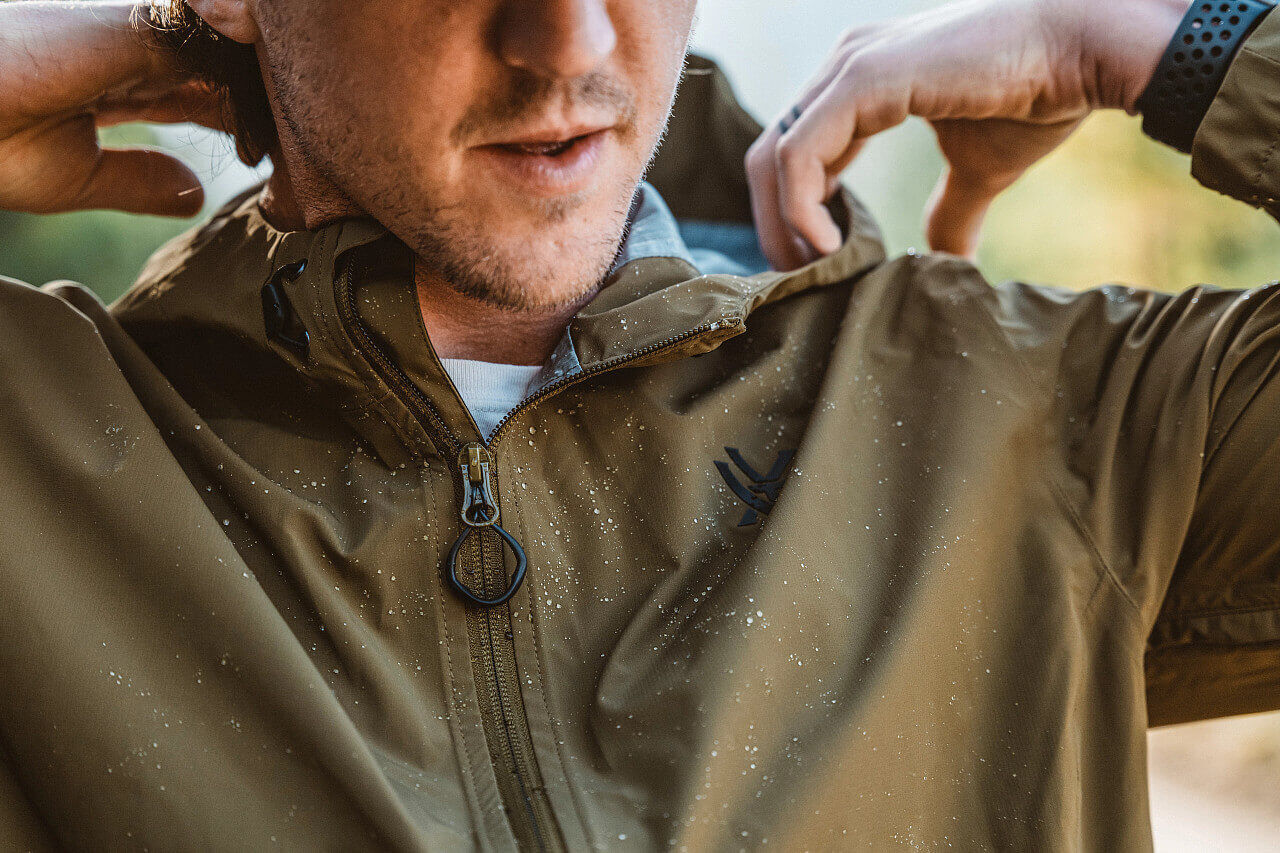 Mann zieht braune wasserabweisende Outdoor-Jacke an