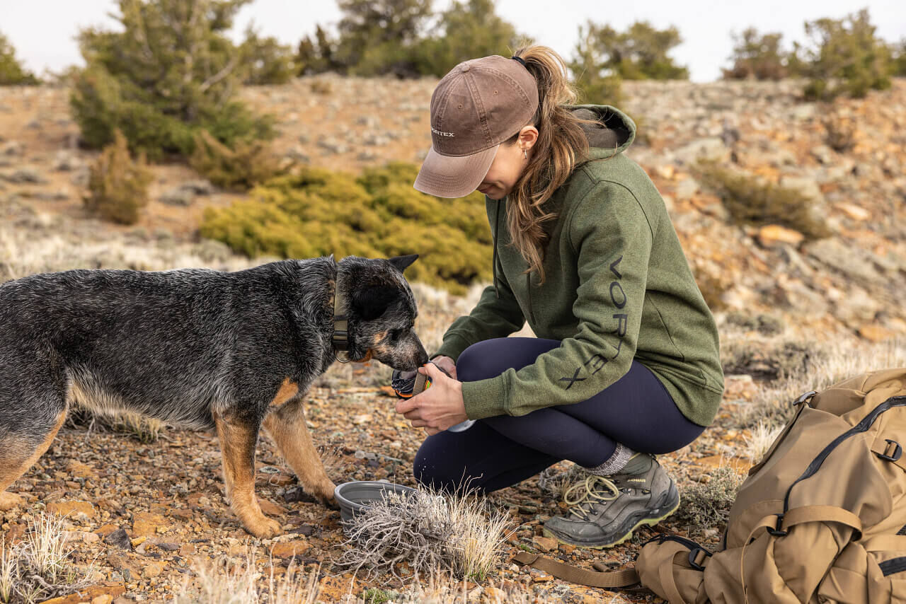 Eine Frau in Outdoor-Kleidung gibt einem Hund Futter während einer Wanderung in einer felsigen Landschaft
