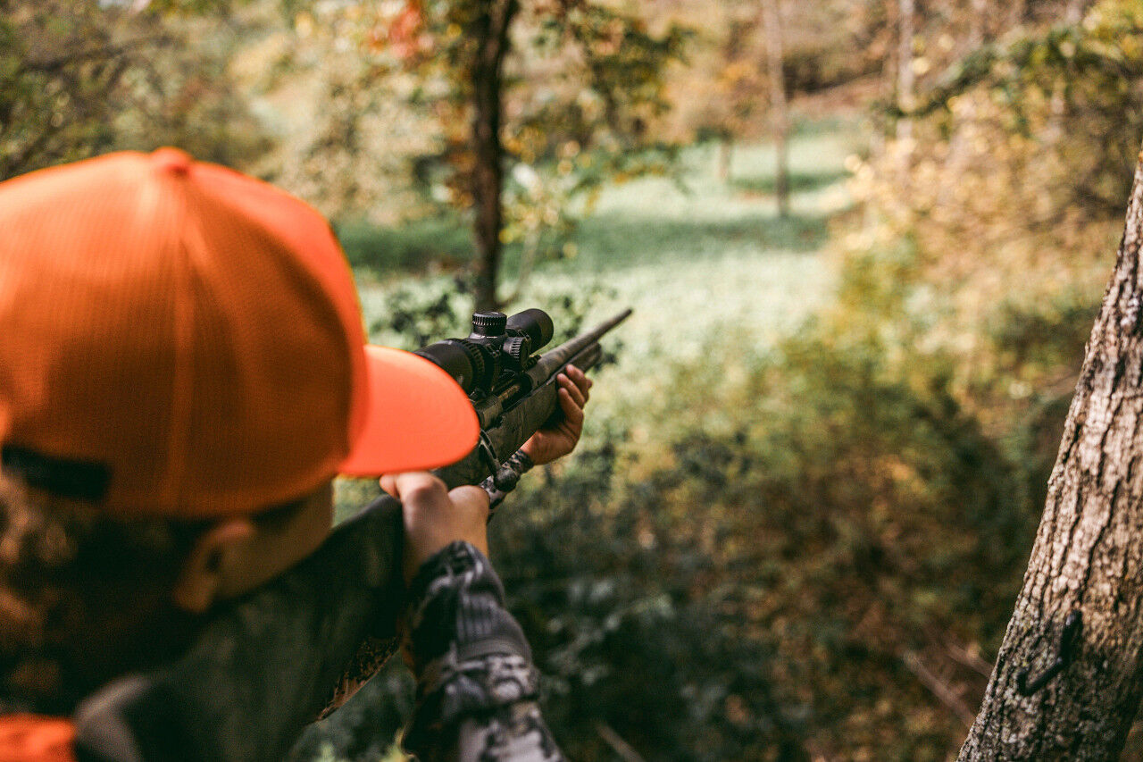 Person mit orangefarbener Kappe zielt mit einem Gewehr im Wald