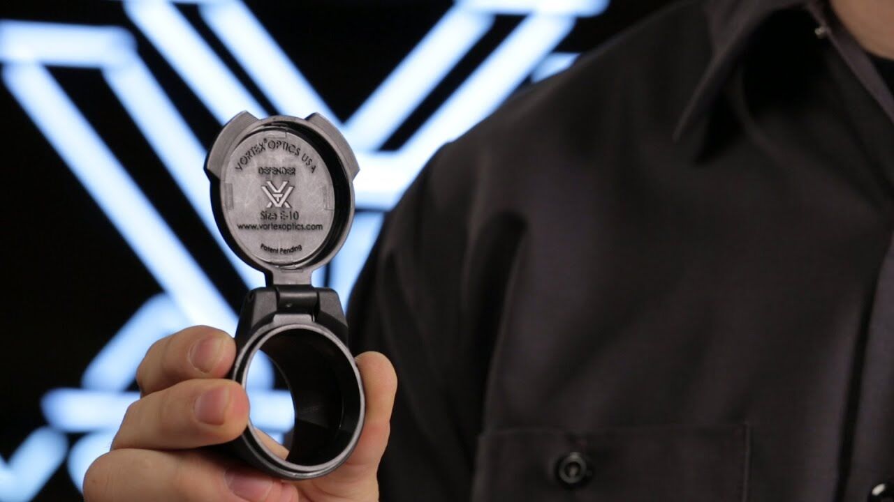Person hält Vortex Optics Schutzkappe, Modell Defender, Größe 8-10 in der Hand.