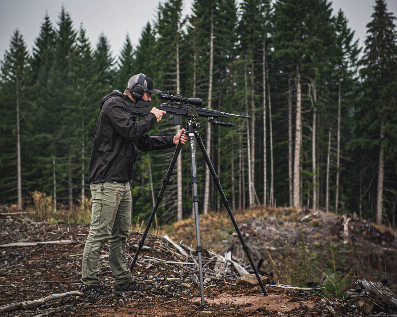 Jäger in Outdoor-Kleidung zielt mit Gewehr auf Stativ im Wald