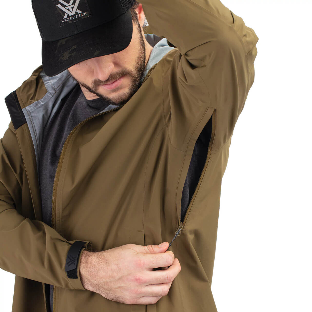 Ein Mann mit schwarzer Kappe öffnet den Reißverschluss seiner braunen Outdoor-Jacke unter dem Arm.