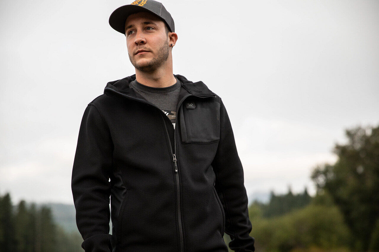 Mann trägt eine schwarze Kapuzenjacke und eine Baseballmütze in einer natürlichen Umgebung