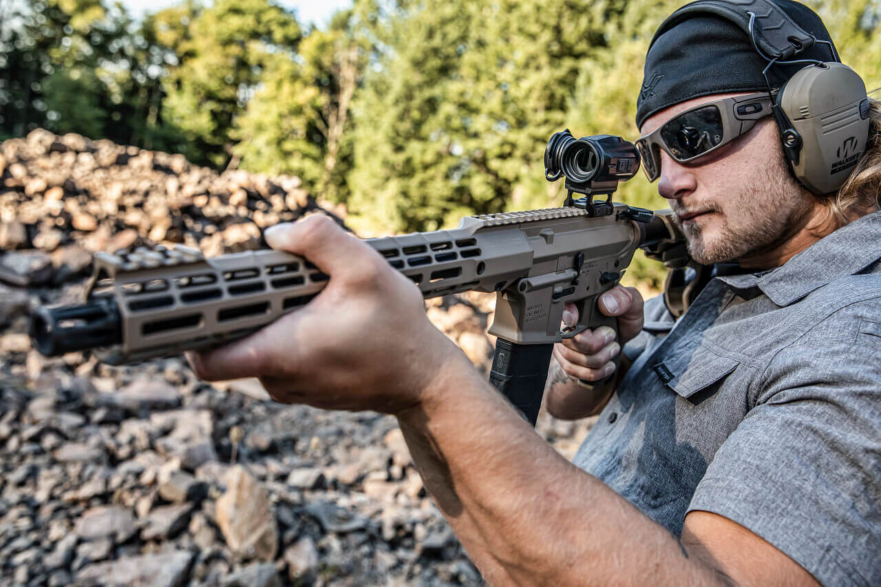 Person mit Schutzbrille und Gehörschutz zielt mit einem taktischen Gewehr auf einem Schießstand im Freien